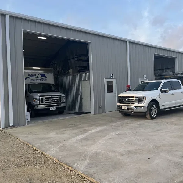 Exterior of a gray metal building with two open garage bays, each with a vehicle parked inside.