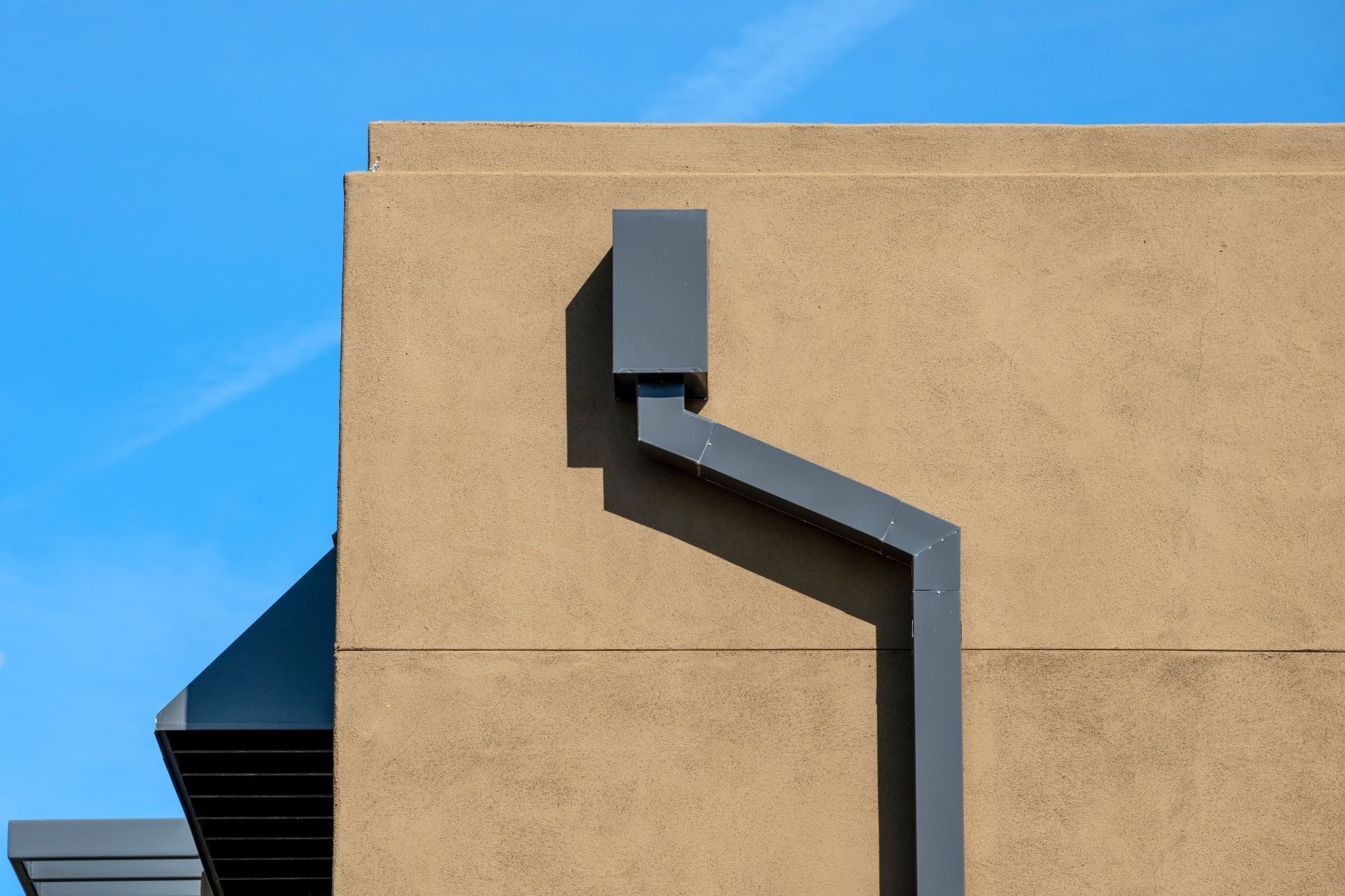 Gray downspout on a tan building against a blue sky.