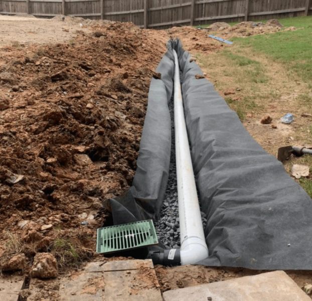 A white pipe is laying in the dirt next to a green drain