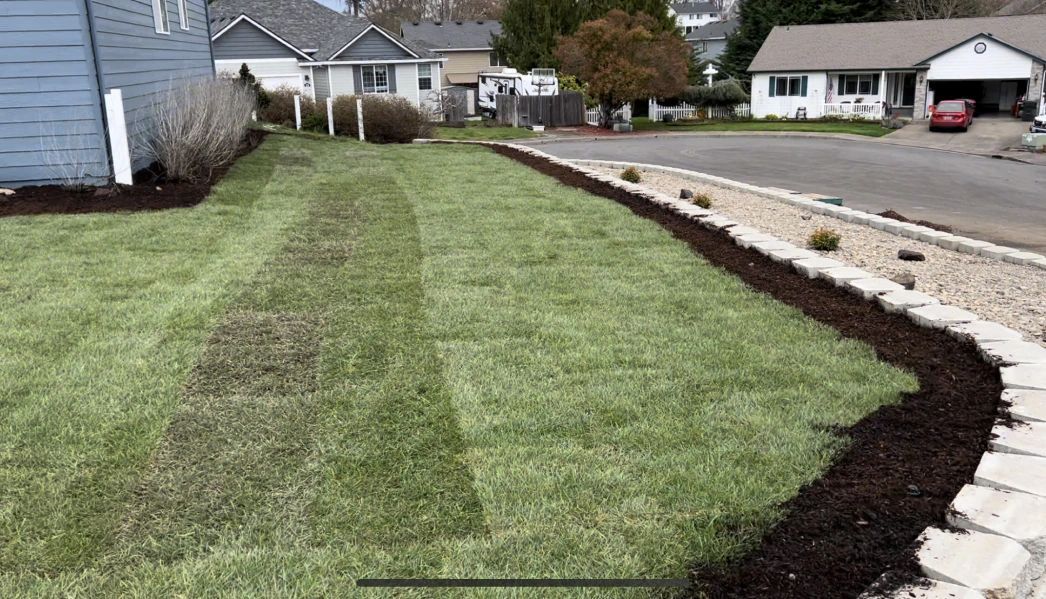 A lush green lawn with a stone wall and a house in the background.