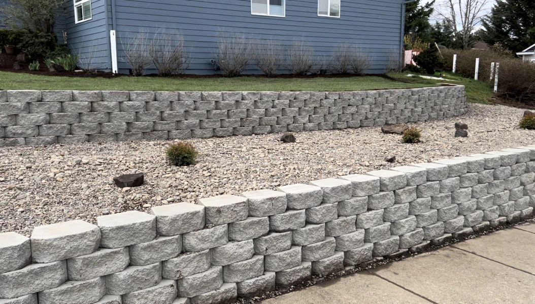 A brick wall is surrounded by gravel in front of a blue house.