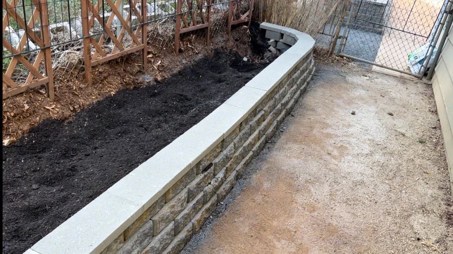 A brick wall is being built in a backyard next to a fence.
