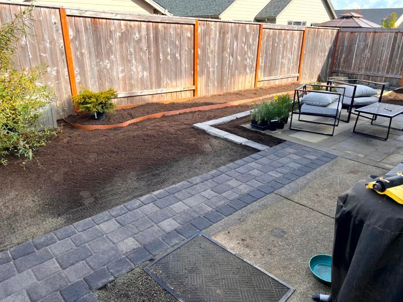 A backyard with a wooden fence and a brick walkway.