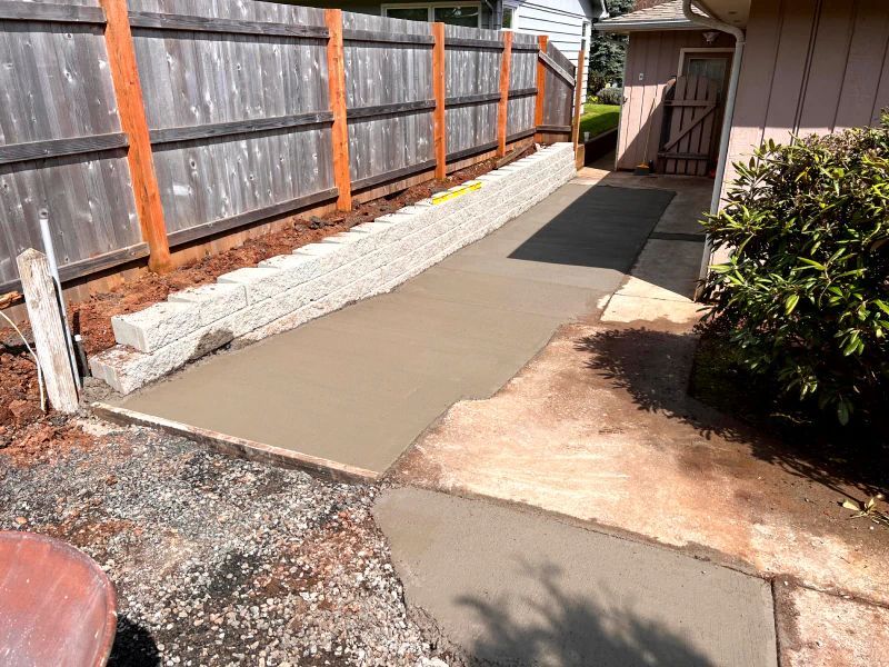 A concrete walkway is being built next to a wooden fence.