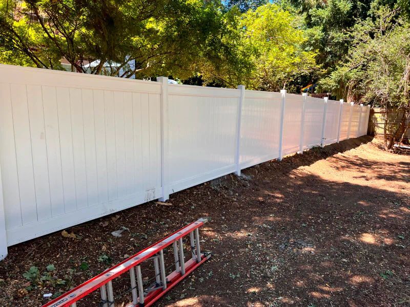 A white vinyl fence with a red ladder leaning against it.