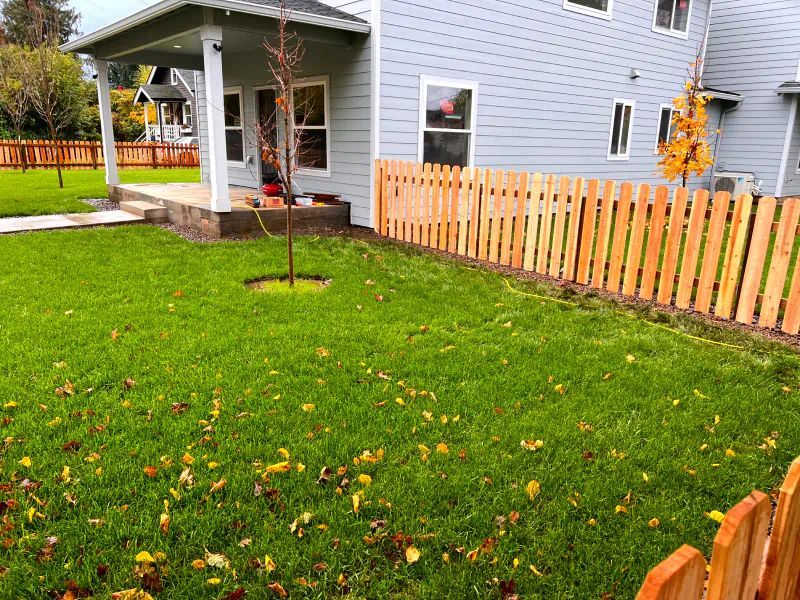 A wooden fence surrounds a lush green lawn in front of a house.