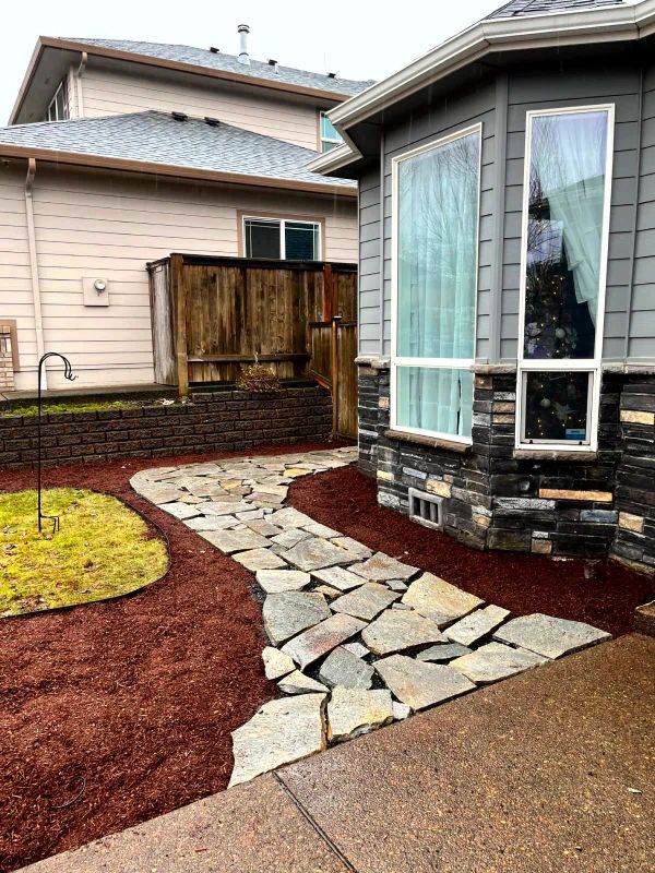 A stone walkway leading to a house with a large window.