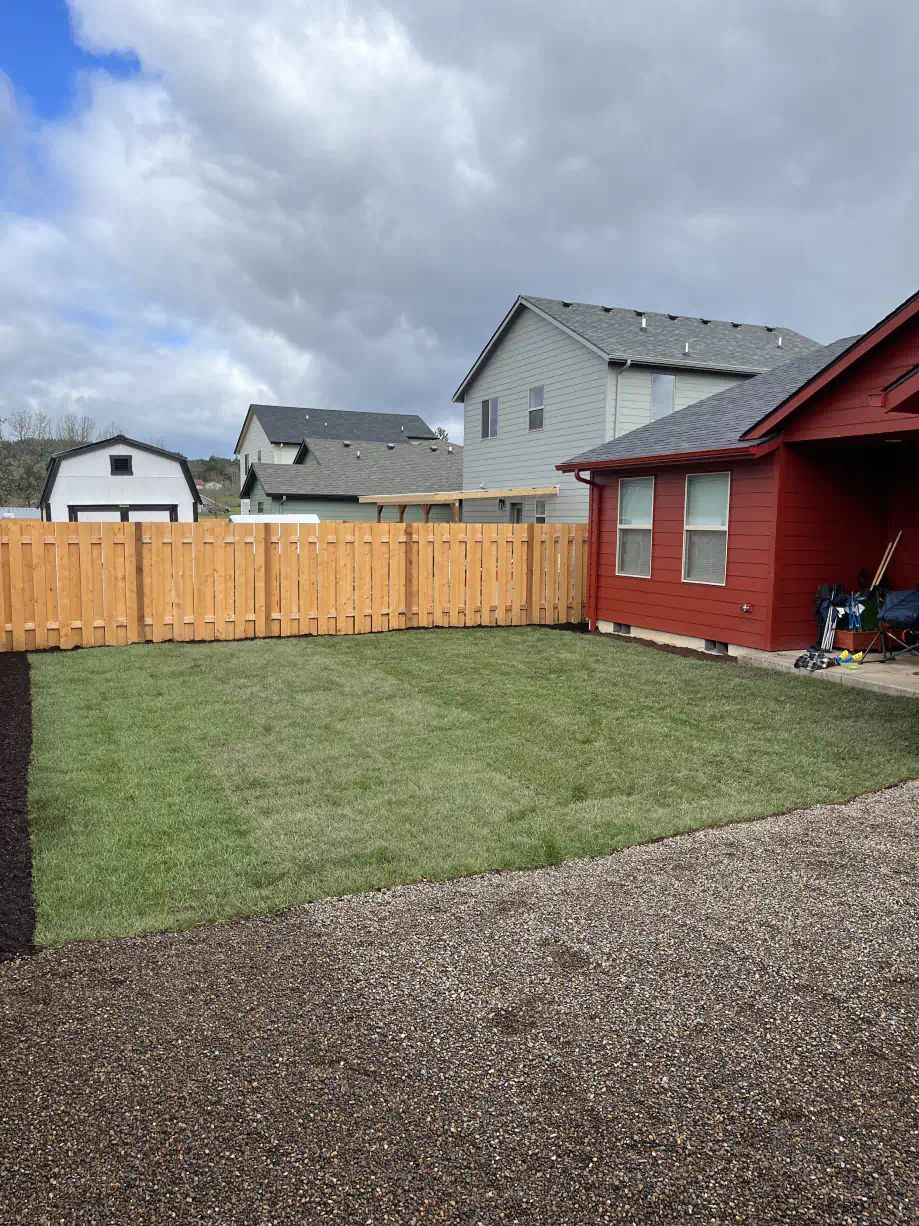A backyard with a wooden fence and a house in the background.
