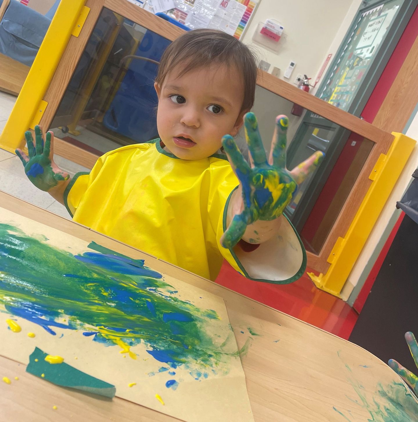 a little boy is sitting at a table with his hands painted green and yellow