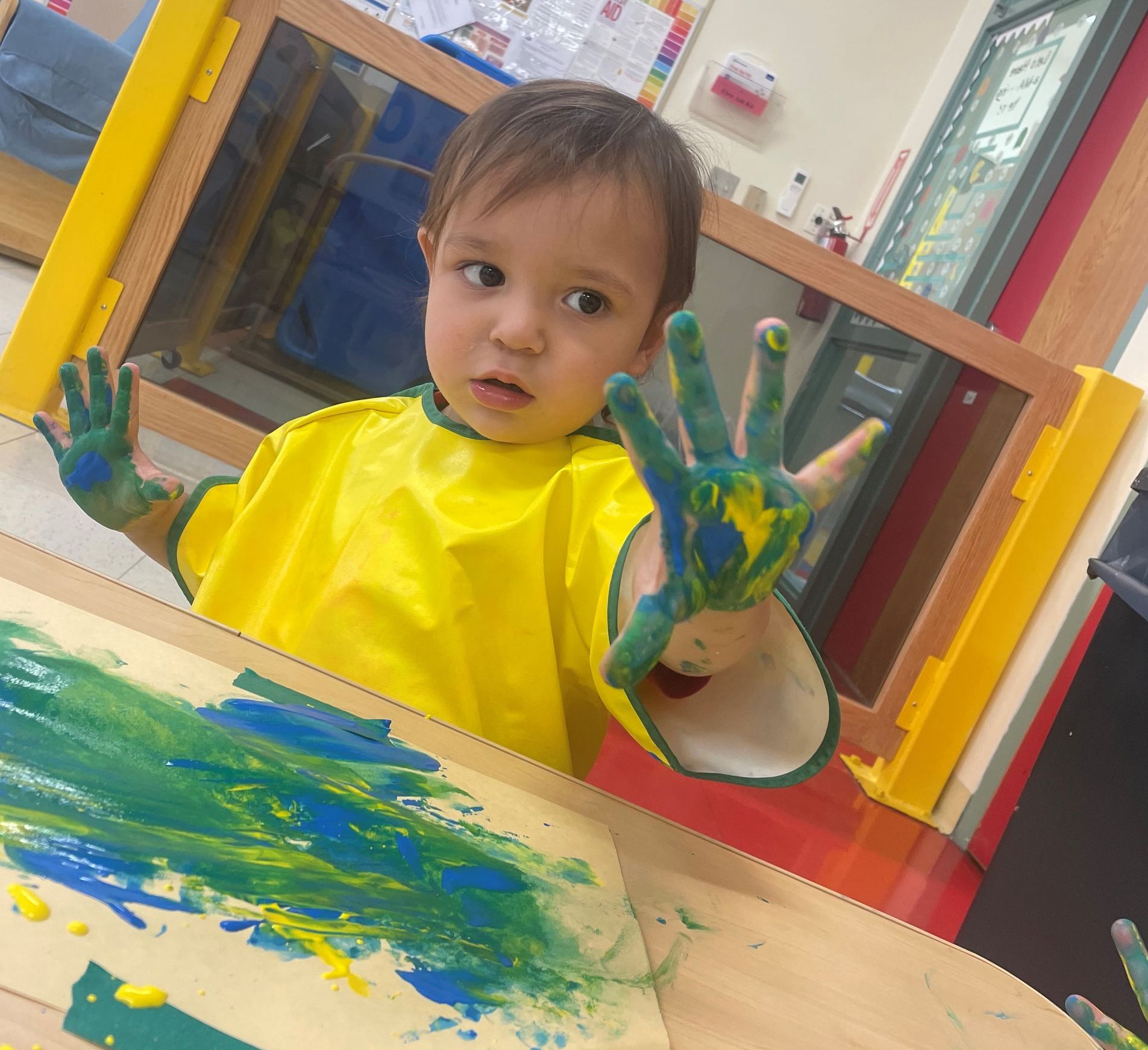 a little boy in a yellow apron has his hands painted green and blue
