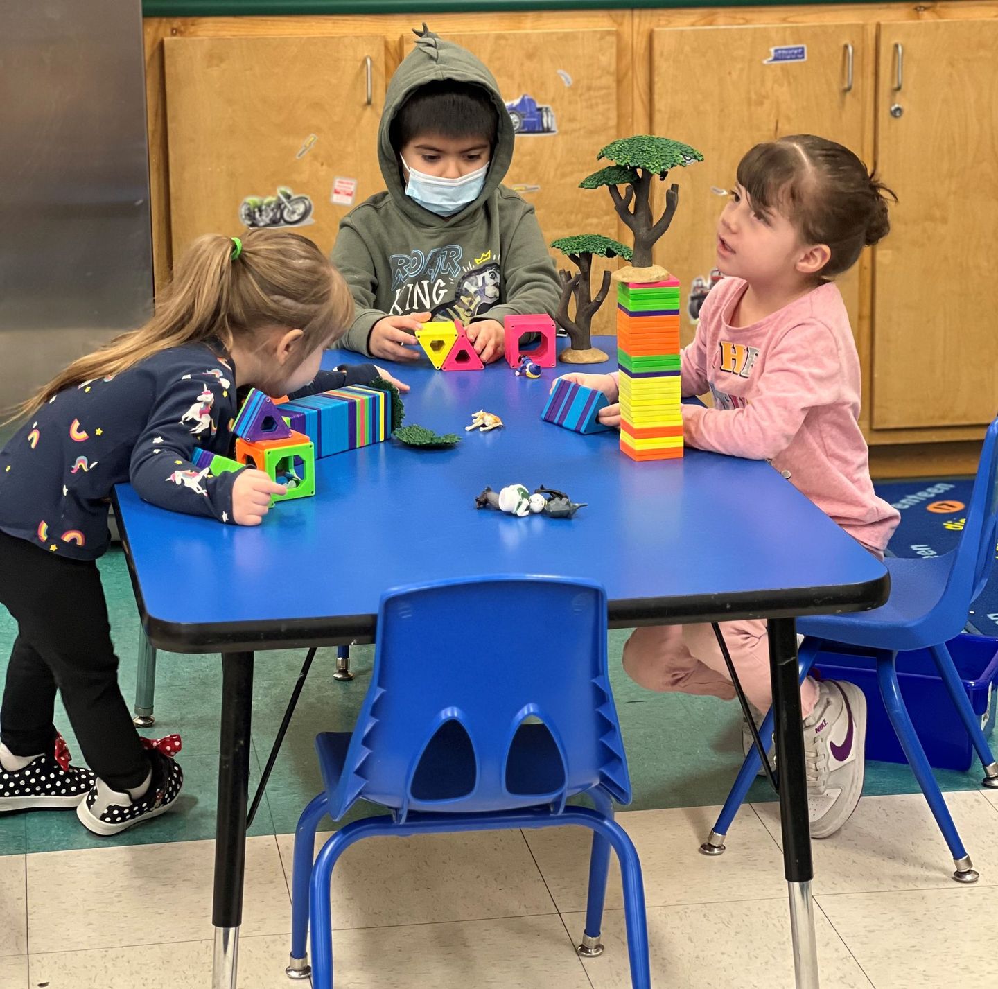 three children are playing with toys at a blue table