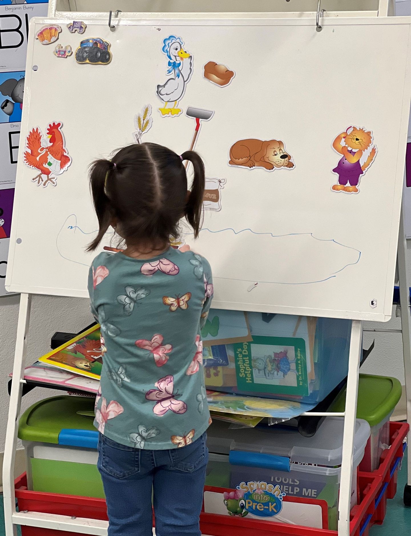 a little girl is standing in front of a white board with stickers on it .