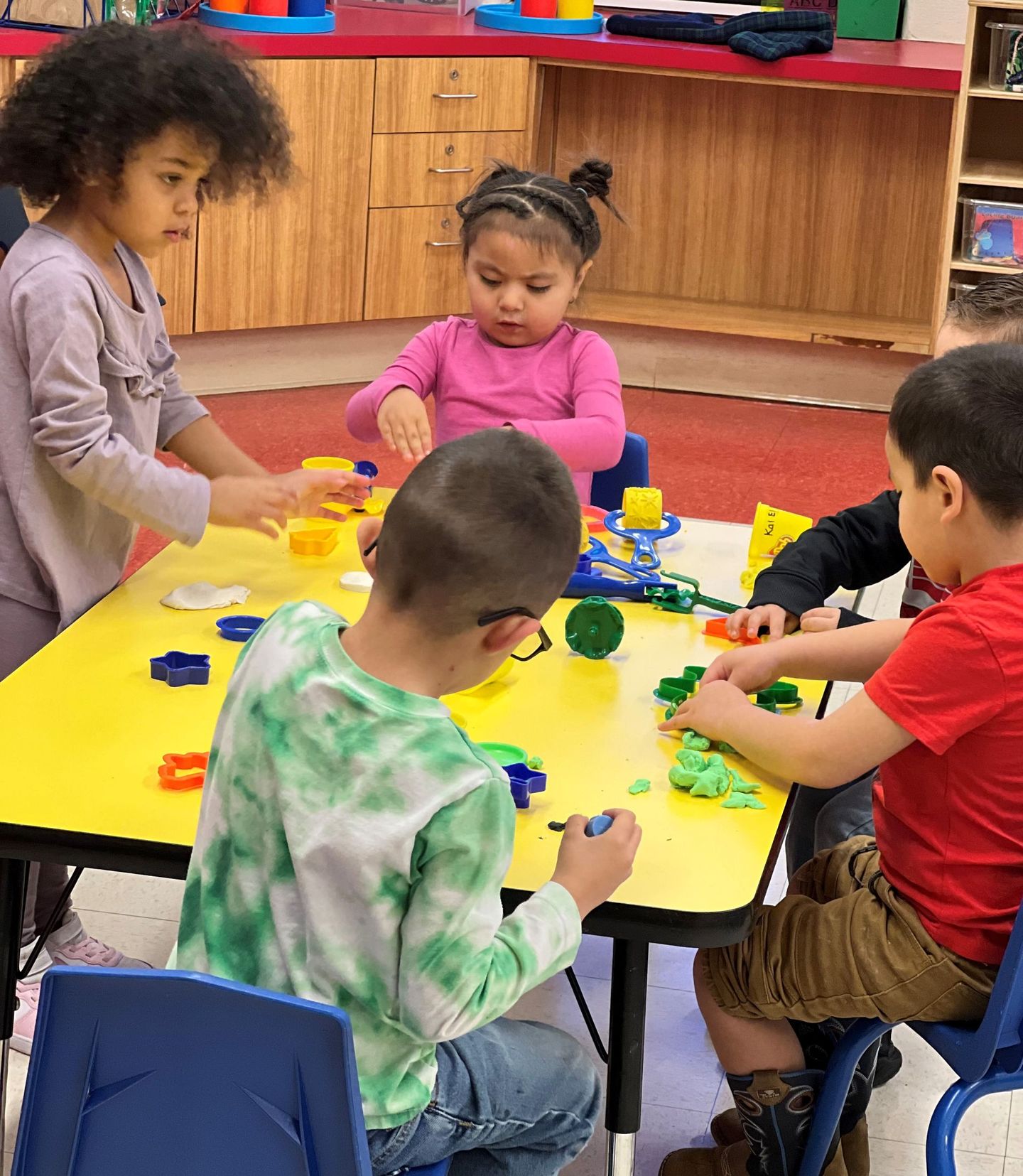 a group of children are playing with play dough at a table .