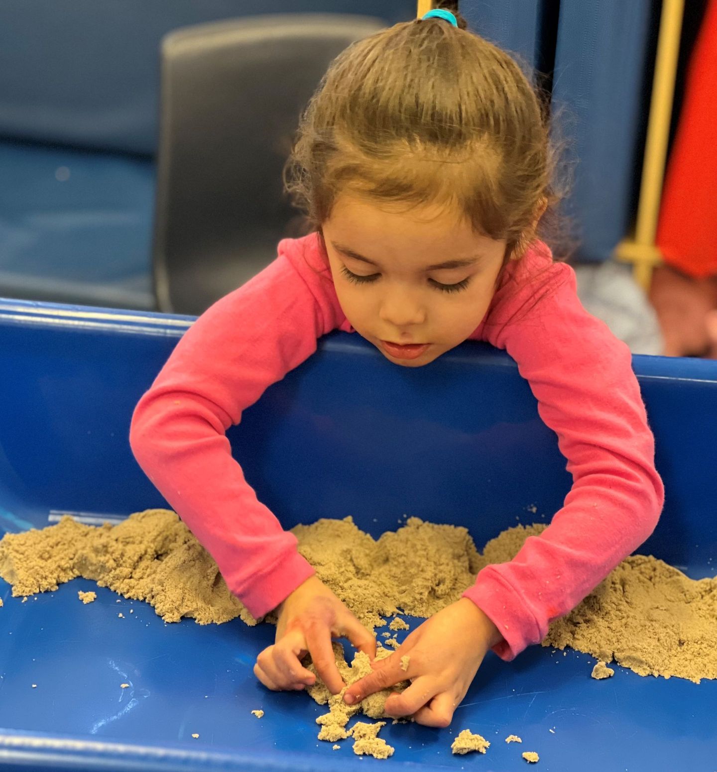 a little girl in a pink shirt is playing with sand