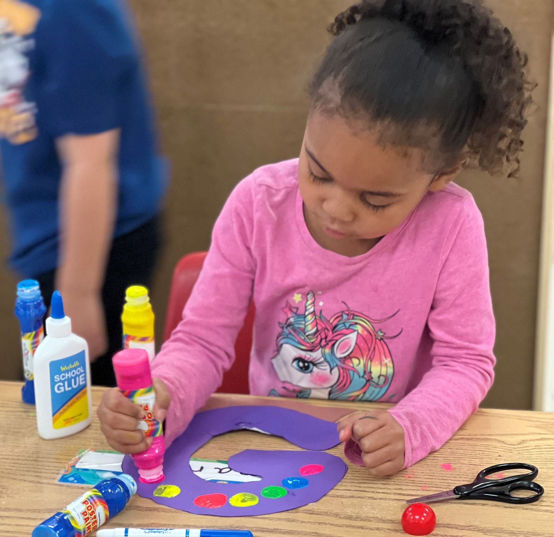 a little girl in a pink shirt is playing with glue