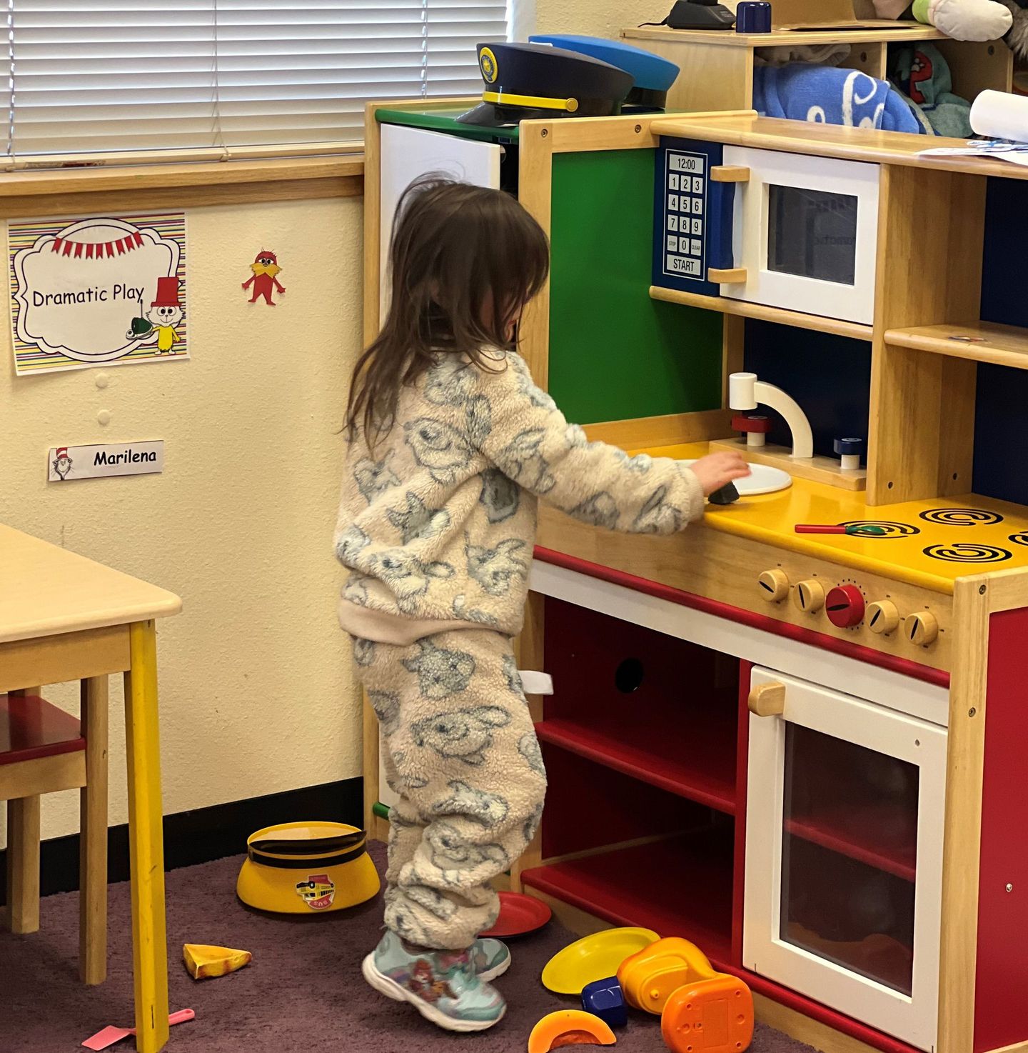 a little girl in pajamas is playing in a play kitchen
