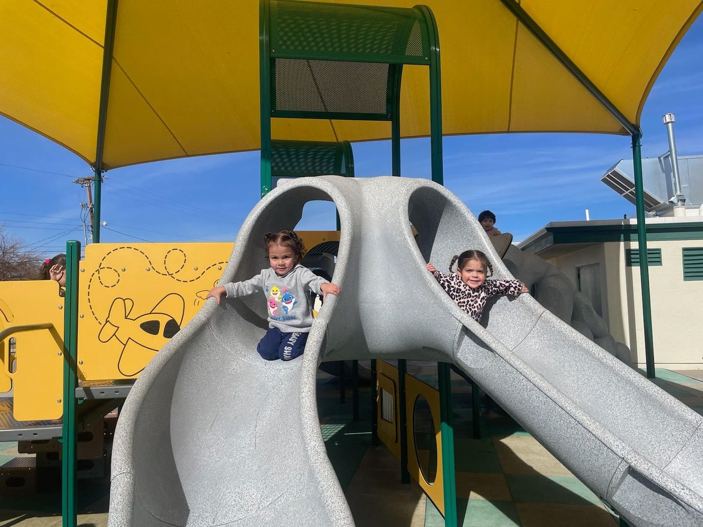 two little girls are playing on a slide at a playground .