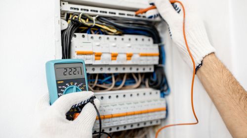 A man is using a multimeter to test an electrical box.