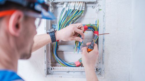 A man is working on an electrical box with a pair of pliers.