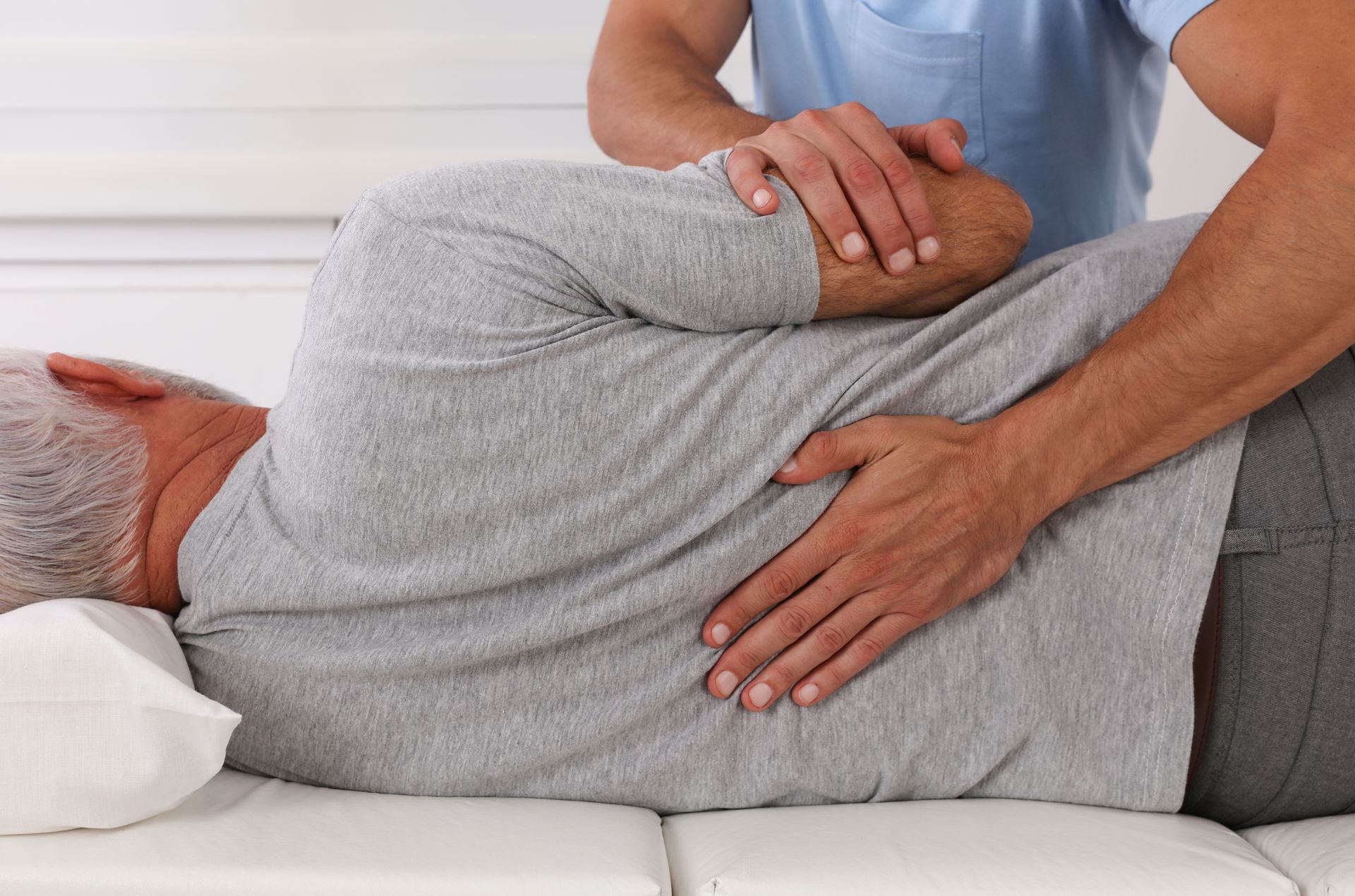 A chiropractor performing a spinal adjustment on an older patient lying on a treatment table. A chiropractor performing a spinal adjustment on an older patient lying on a treatment table.