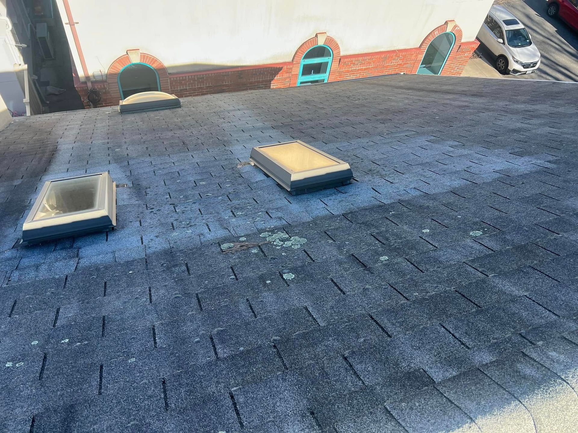A rooftop with three skylights, covered in dark asphalt shingles, and signs of moss growth.
