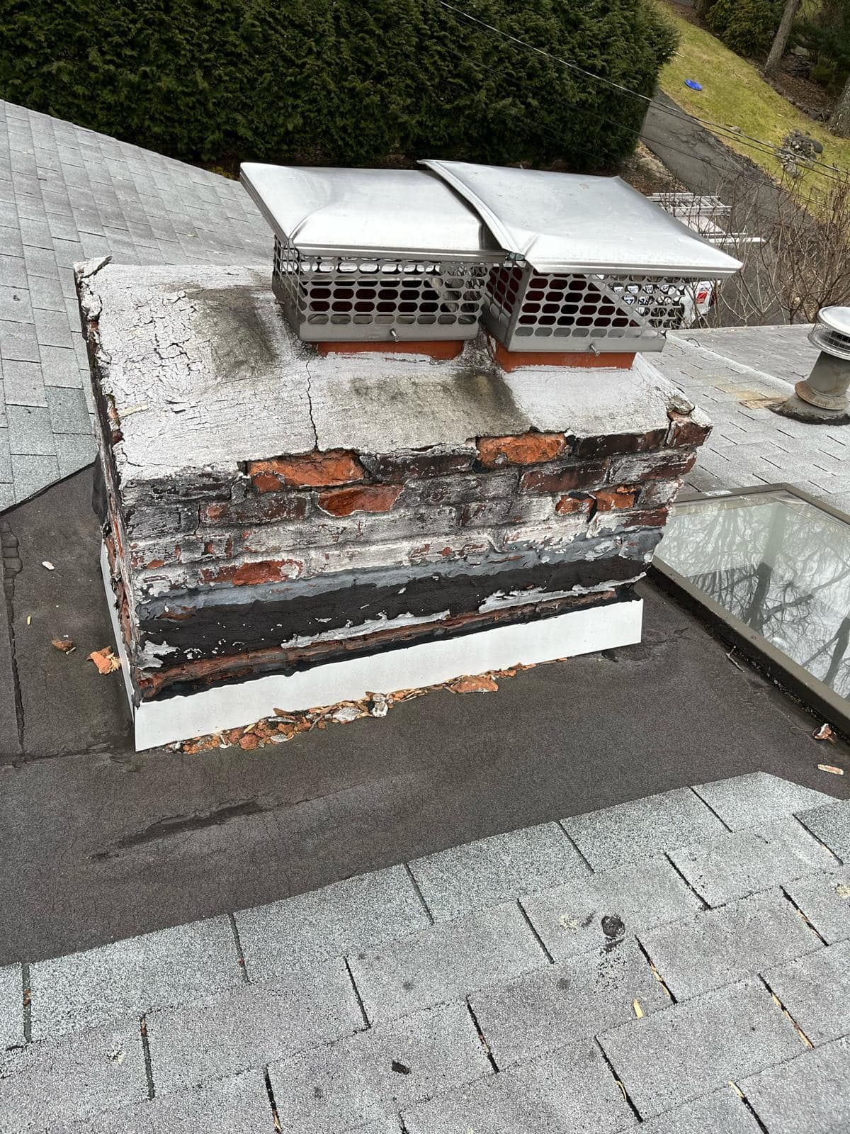 Chimney with brick and weathered appearance, featuring two metal chimney caps on a shingled roof.