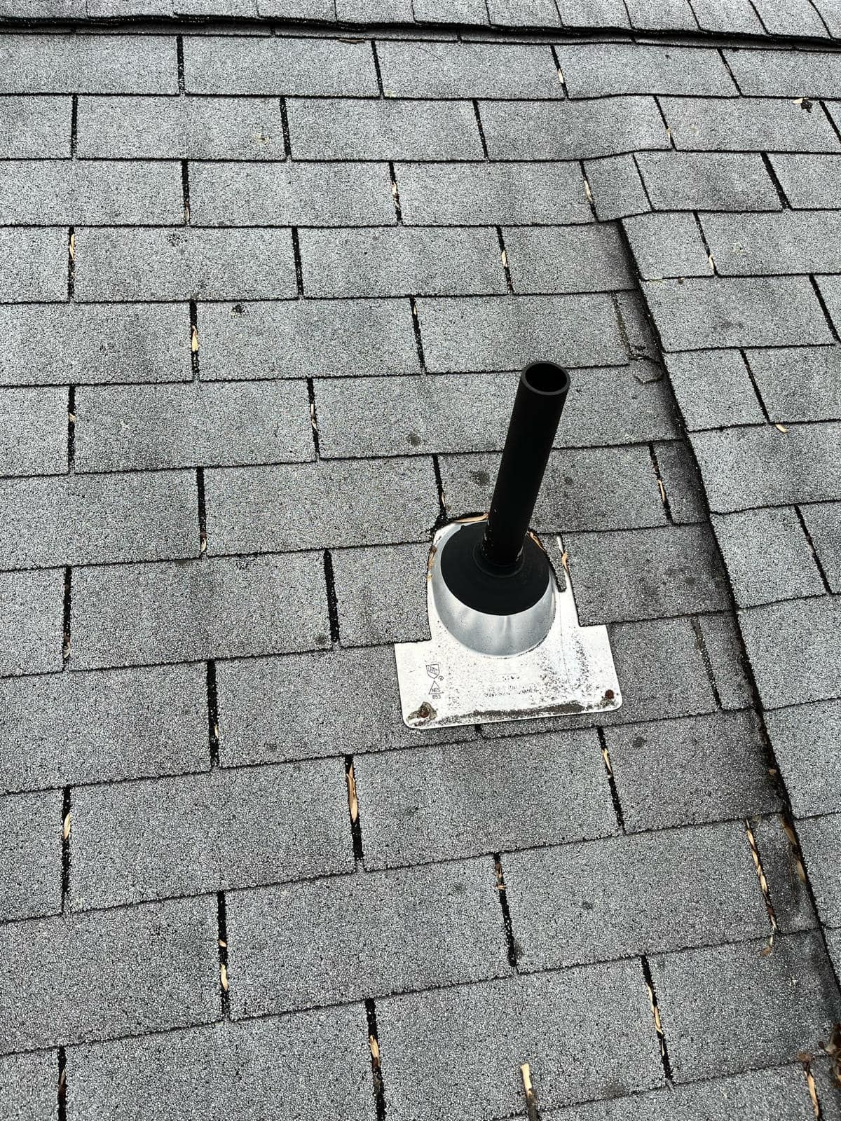 Black vent pipe protruding from a gray shingle roof.