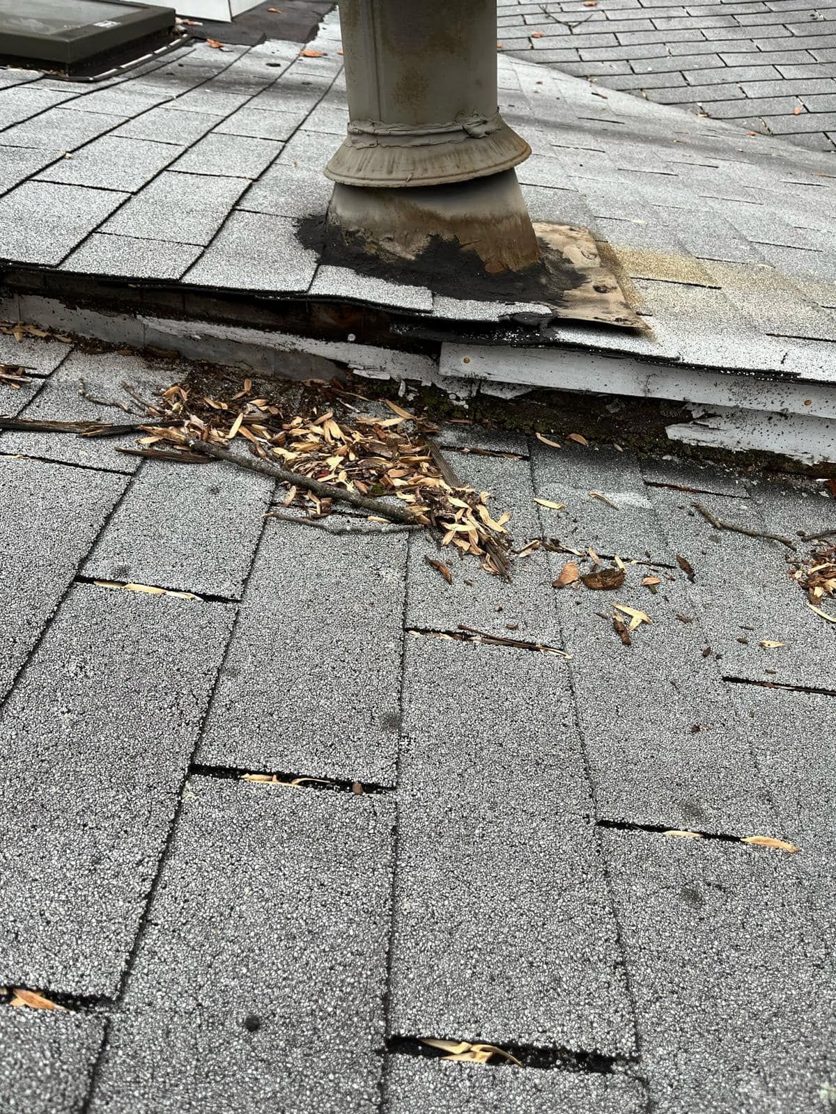 Damaged asphalt shingles around a roof vent with debris and missing pieces.