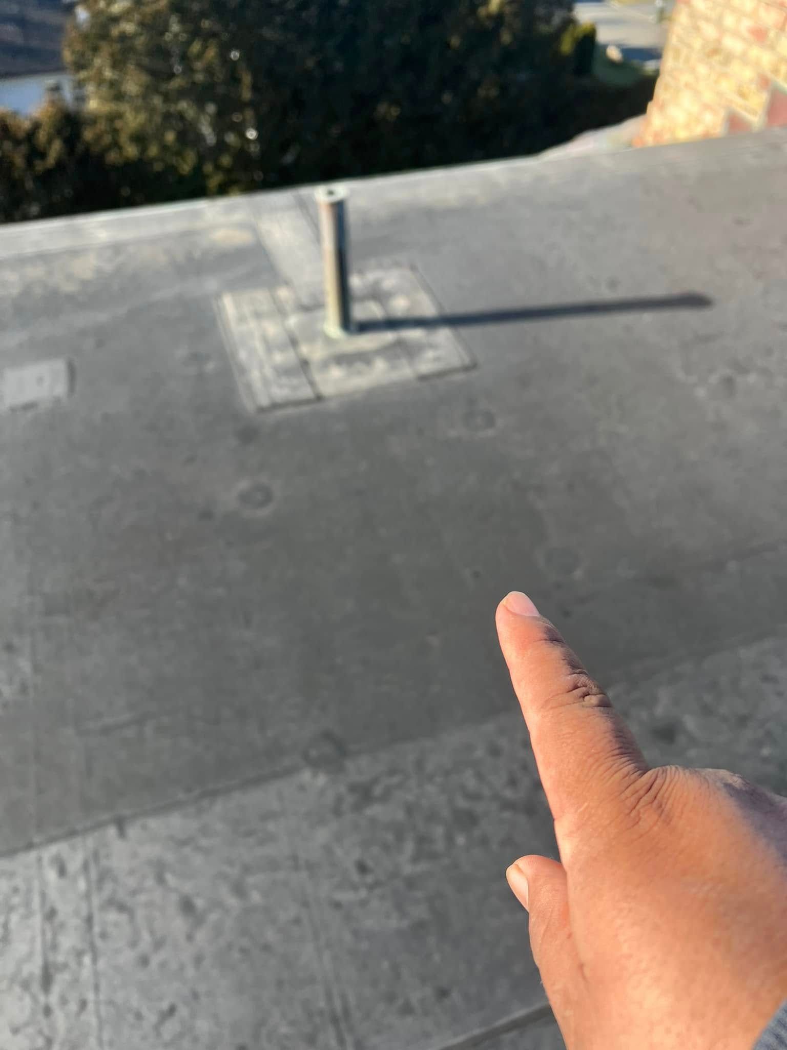 A finger points to a flat, gray surface with a shadow cast by a vertical pipe in the sun.