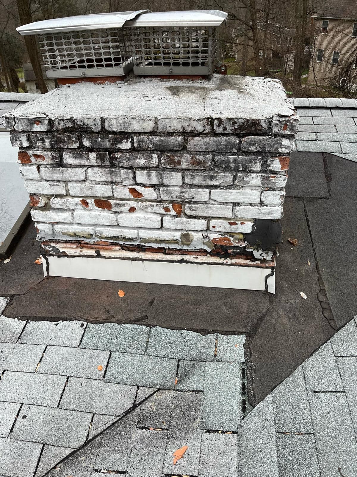 Brick chimney on a gray shingled roof, showing signs of weathering and discoloration.