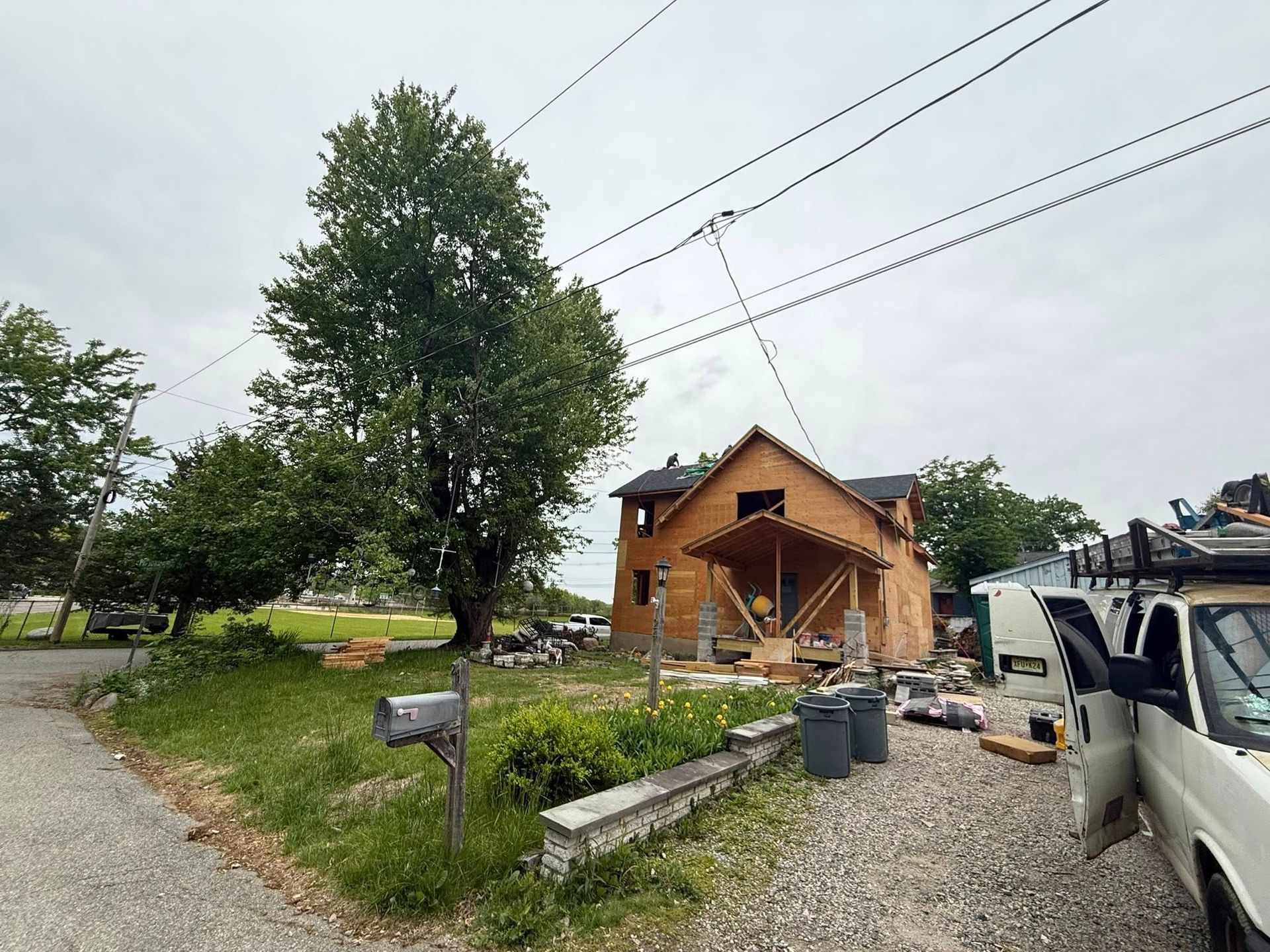 House under construction with exposed wooden frame, overhead power lines, and a parked van.