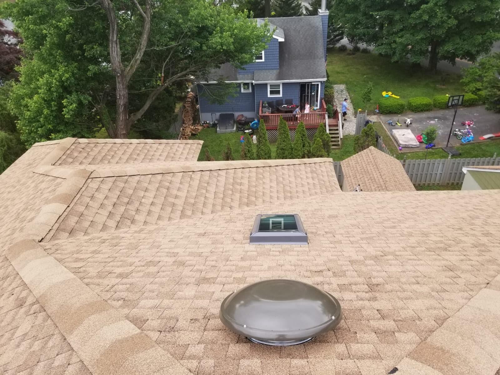 Overhead view of a house roof with a skylight and a solar tube. Other houses and trees in the background.