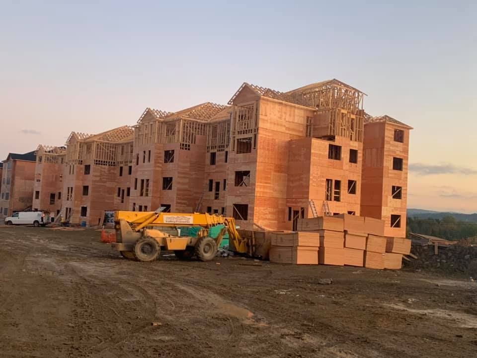Building under construction with wooden frame; yellow forklift on dirt.