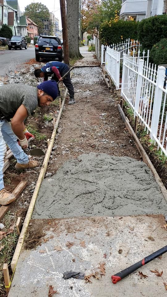 Three people working on a concrete sidewalk. They are leveling and pouring cement in a residential area.