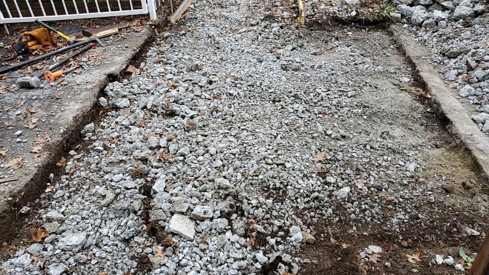 Gravel pathway under construction, bordered by concrete and dirt, with tools visible on the side.
