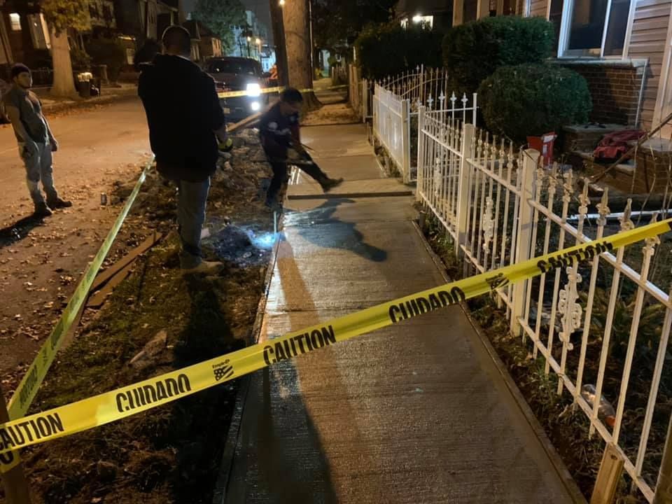 Sidewalk damage with caution tape. People stand near a damaged area with a newly poured section.