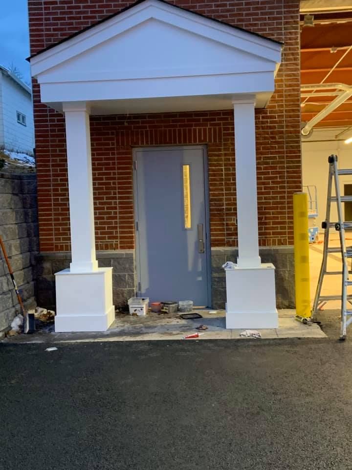 Brick building exterior with white columns and doorway. Tools and ladder nearby.