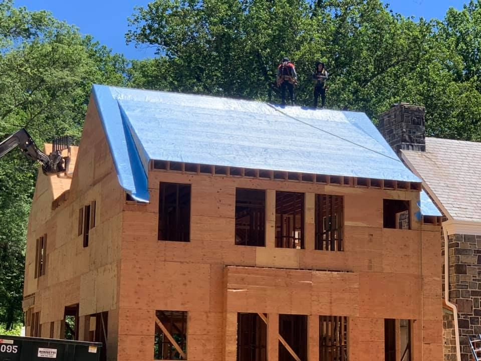 Construction workers on a roof, covering it with blue material. Two-story wooden house under construction.