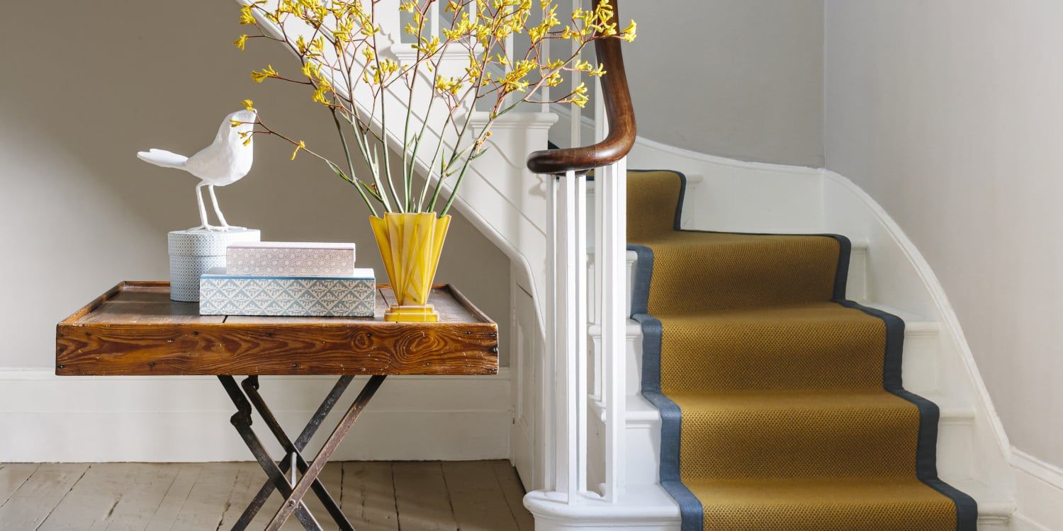 A staircase with a yellow carpet and a table with a vase of flowers on it.