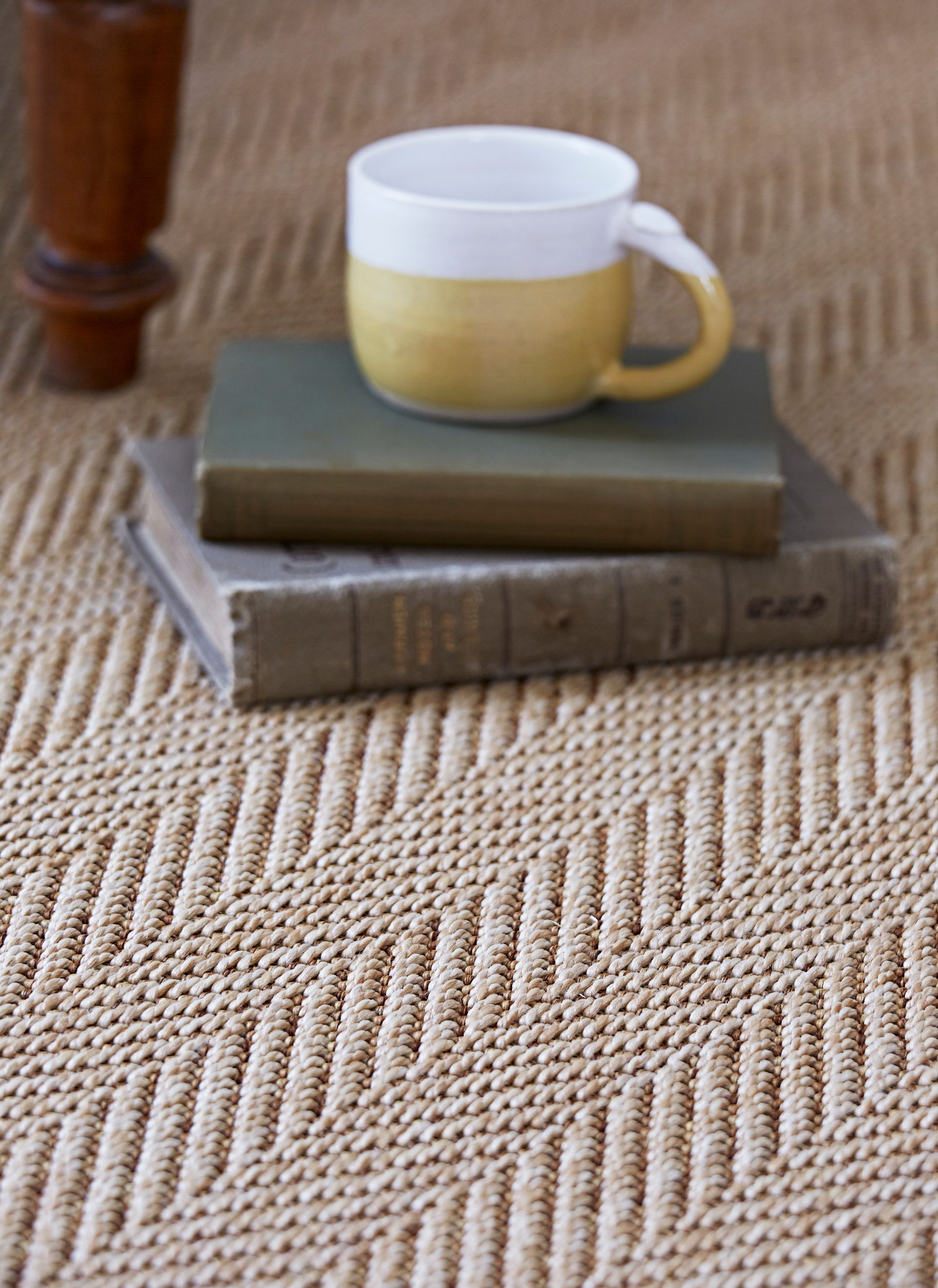 A stack of books and a cup on a rug