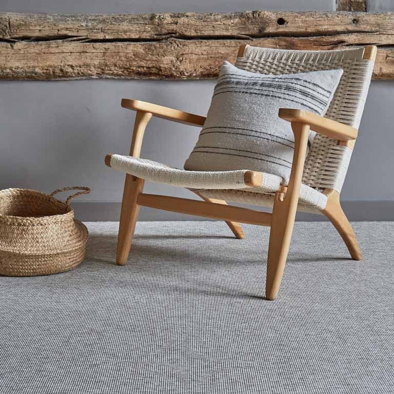 A chair with a pillow on it is sitting on a rug next to a basket.