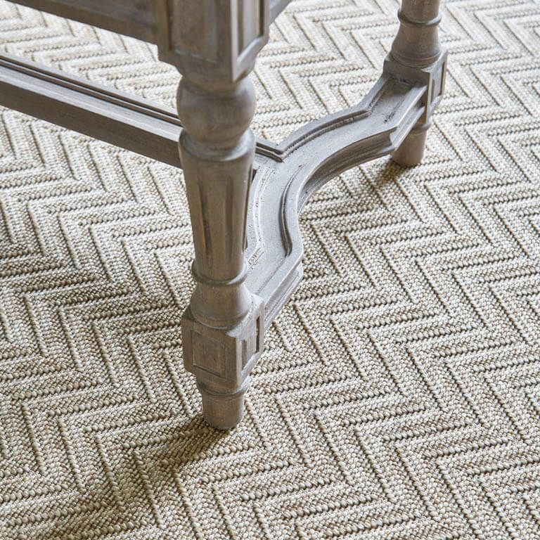 A wooden table is sitting on a rug with a herringbone pattern.