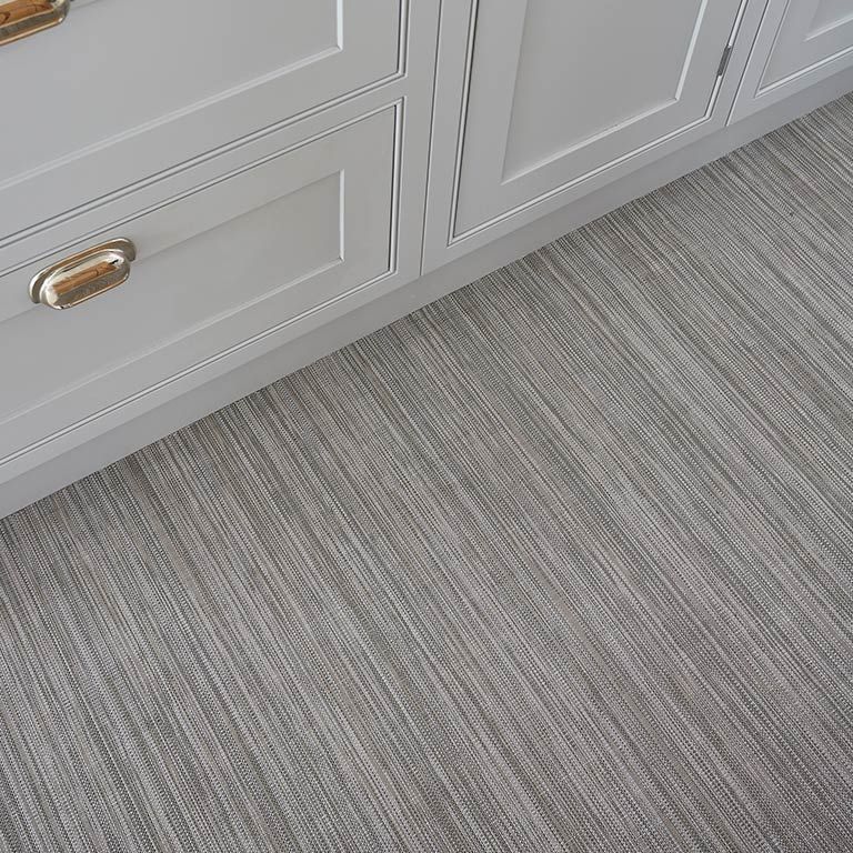 A kitchen floor with a striped carpet and white cabinets.