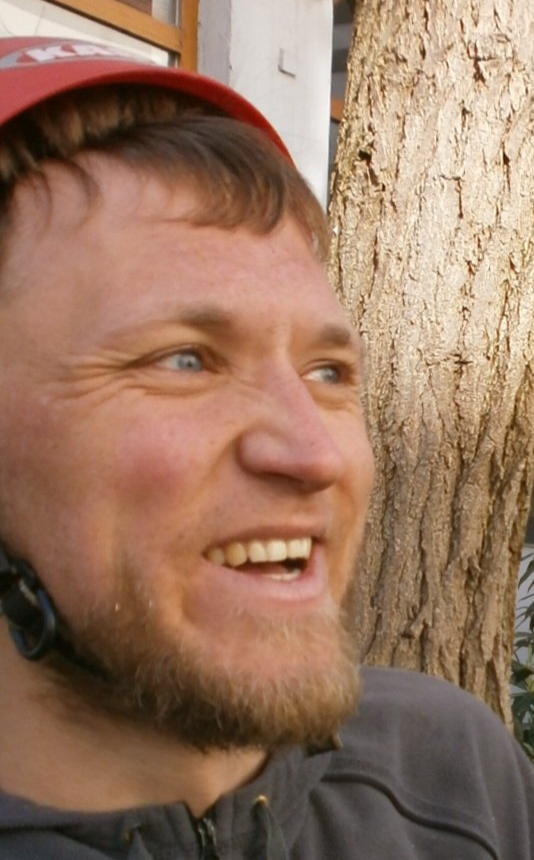 Mann mit Helm lächelt begeistert neben Baum
