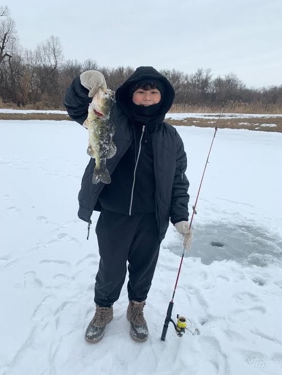 Person on snowy ice holding a fish and a fishing rod beside a frozen lake