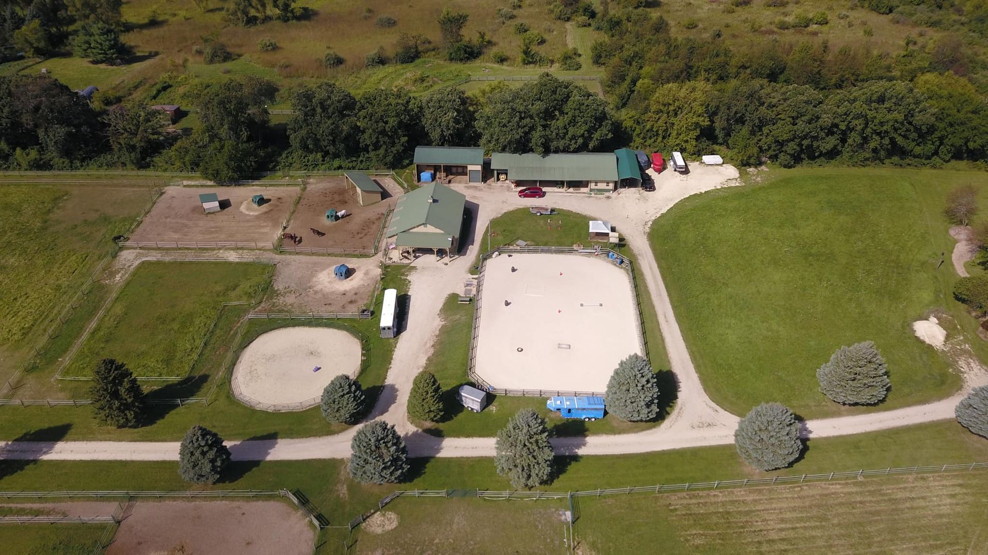 Aerial view of a farm with barns, a large white-roofed building, and fenced grassy fields.
