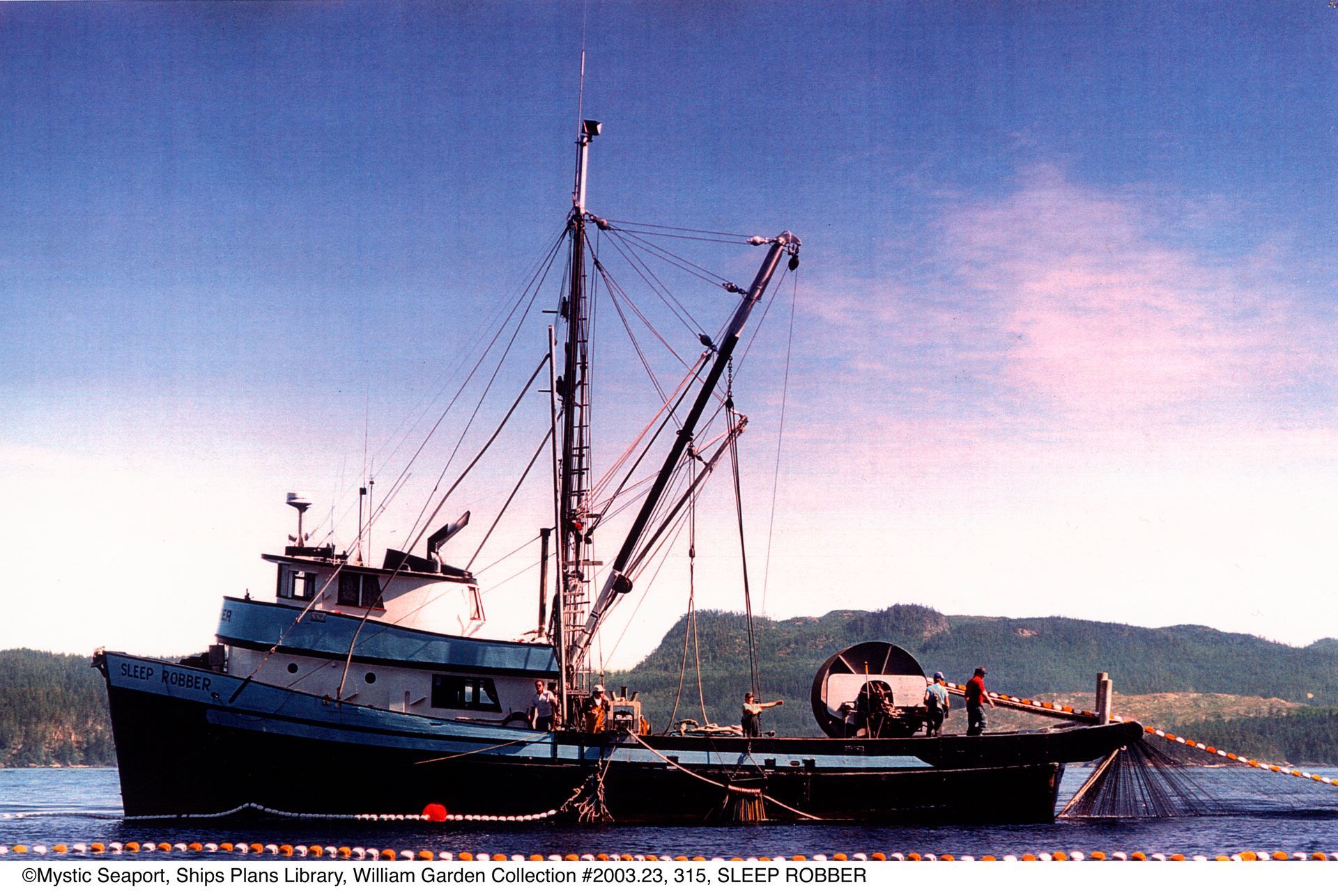 A large fishing boat is docked in the water with mountains in the background