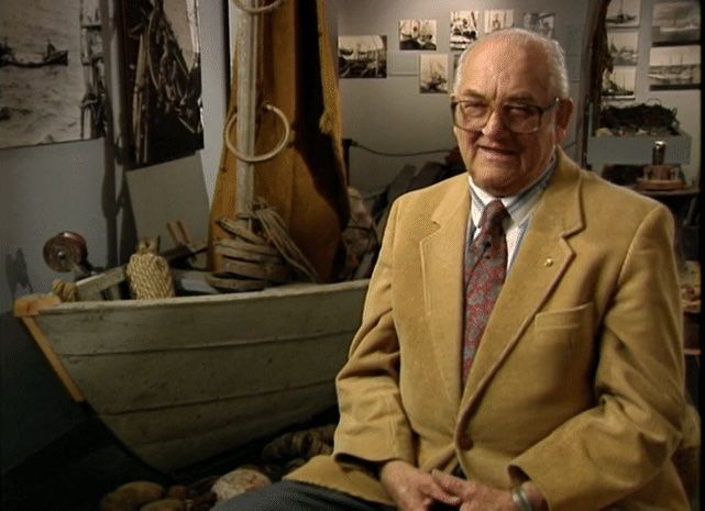 A man in a suit and tie is sitting in front of a boat