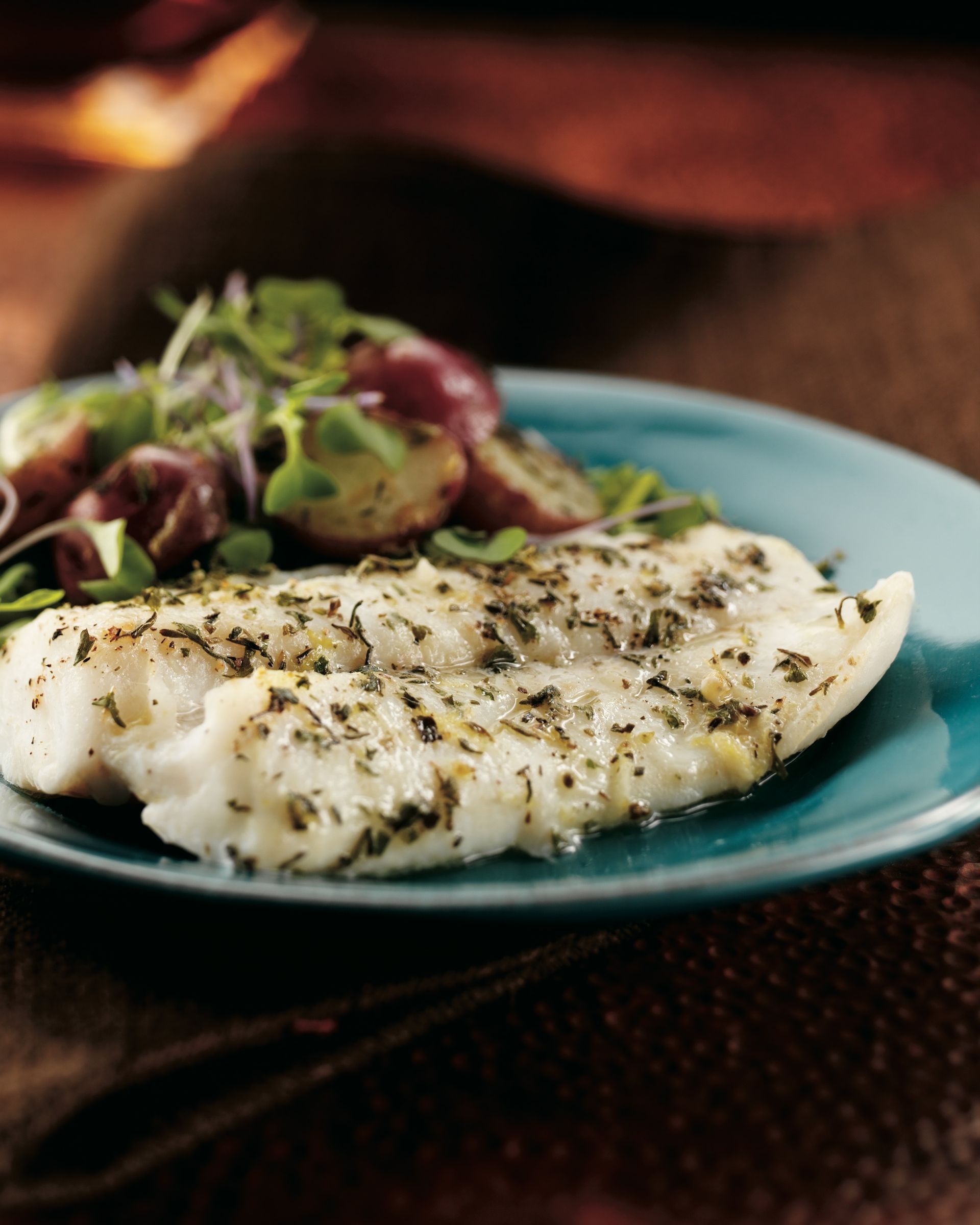 A blue plate topped with fish and vegetables on a table.