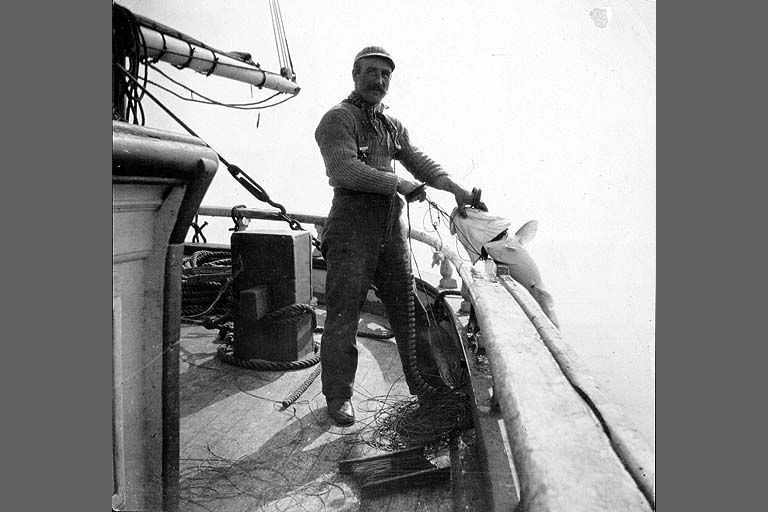 A man is standing on the deck of a boat holding a rope.